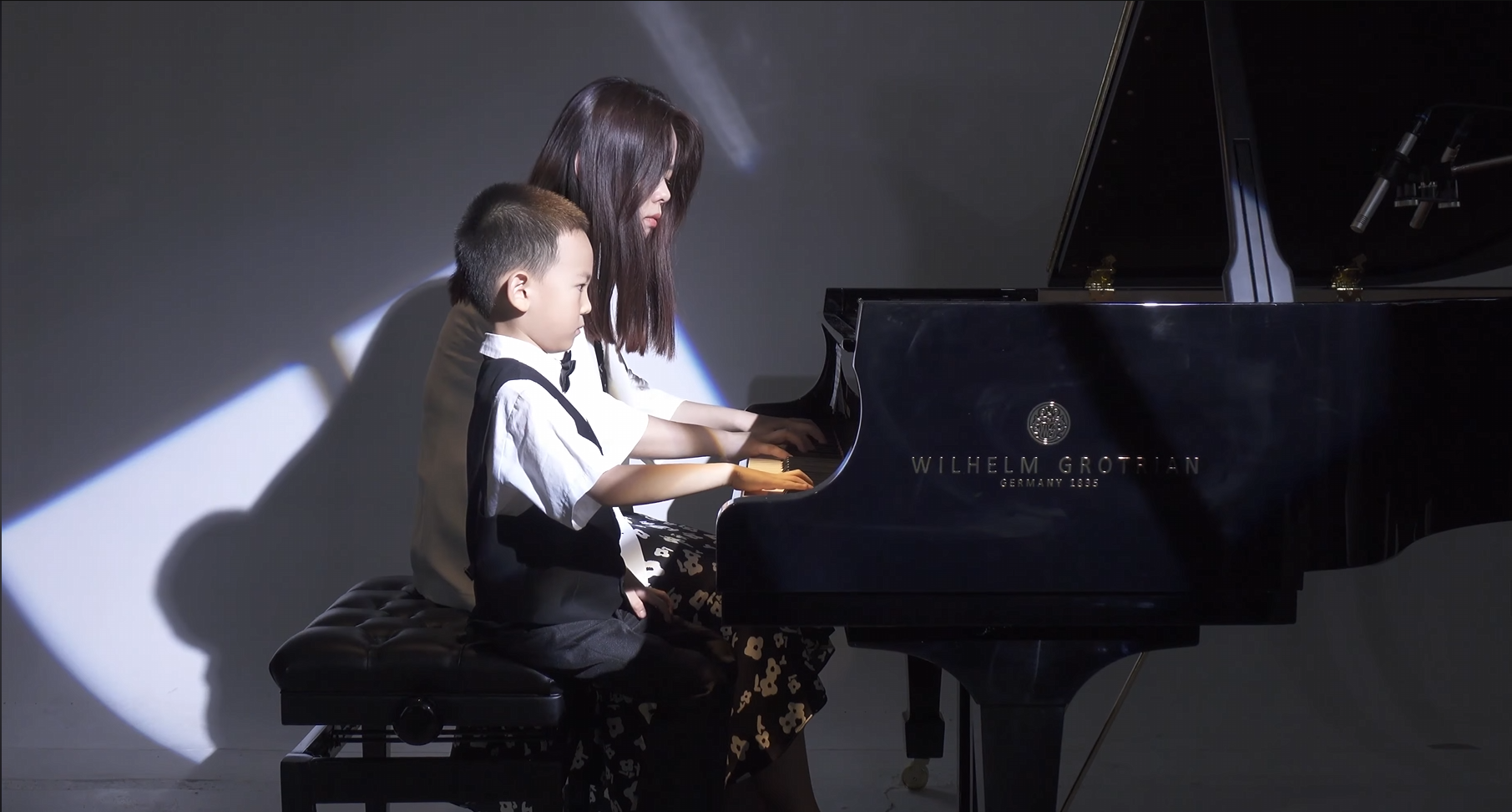 A piano teacher and young student performing together at a grand piano